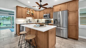 A kitchen with wooden cabinets, a stainless steel refrigerator, a microwave, and a ceiling fan. - Heated Pool & Hot Tub, Walk to Beach, Fully Equipped. Free Bikes. Grill. (Naples)