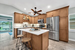 A kitchen with wooden cabinets, a stainless steel refrigerator, a microwave, and a ceiling fan. - Heated Pool & Hot Tub, Walk to Beach, Fully Equipped. Free Bikes. Grill. (Naples)