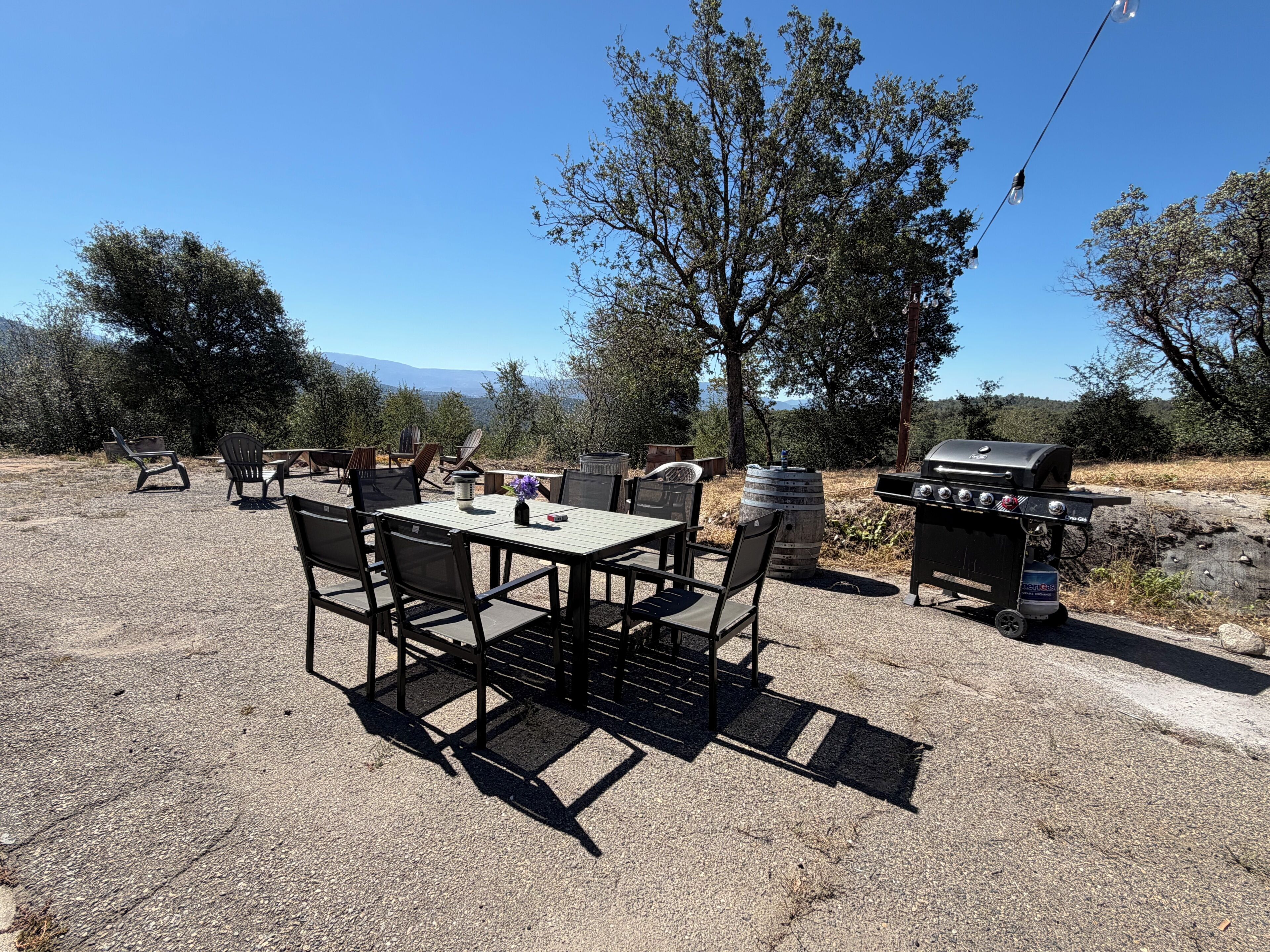 An outdoor patio with a table and chairs, a barbecue grill, and a scenic view of trees and mountains.