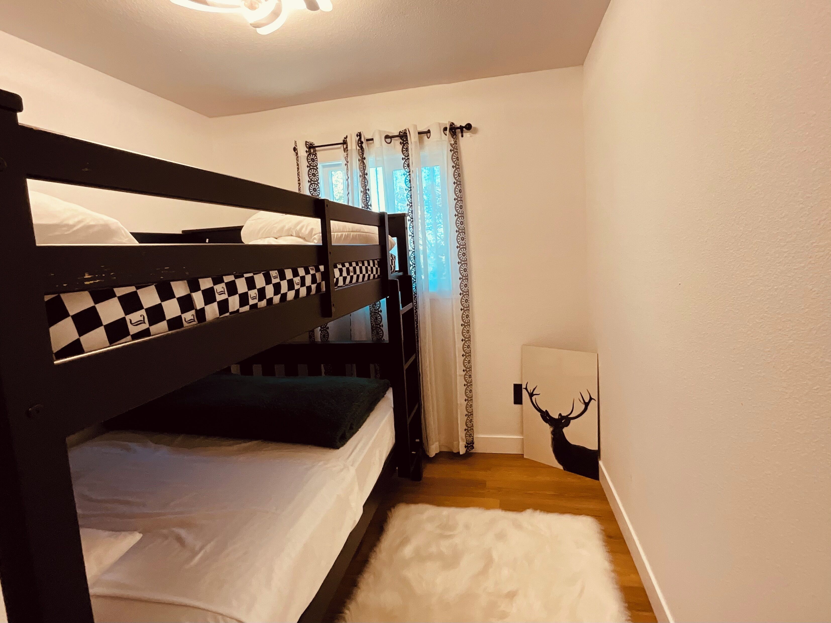 A bunk bed room with a checkered headboard, a white furry rug, and a deer wall art.