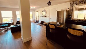 A spacious living area with a dining table, chairs, a sofa, and a kitchen area with a refrigerator and stove. - Cozy 3-bedroom cabin in charming North Fork with AC (North Fork)