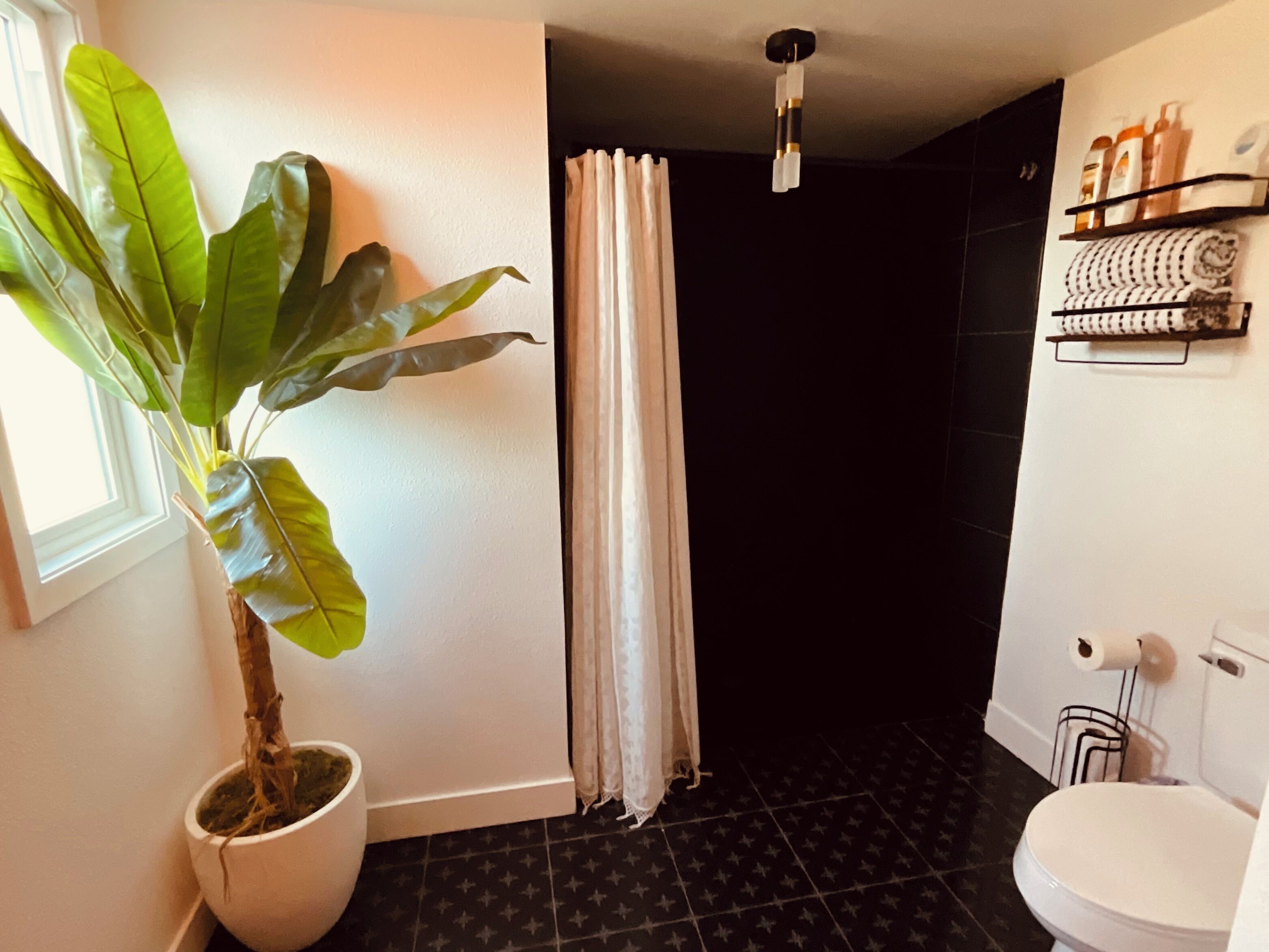 Ein Badezimmer mit Topfpflanze, Duschvorhang, Toilette und Ablagefläche für Toilettenartikel.