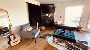 A living room with a fireplace, a sofa, a coffee table, a guitar, and a television. - Cozy 3-bedroom cabin in charming North Fork with AC (North Fork)