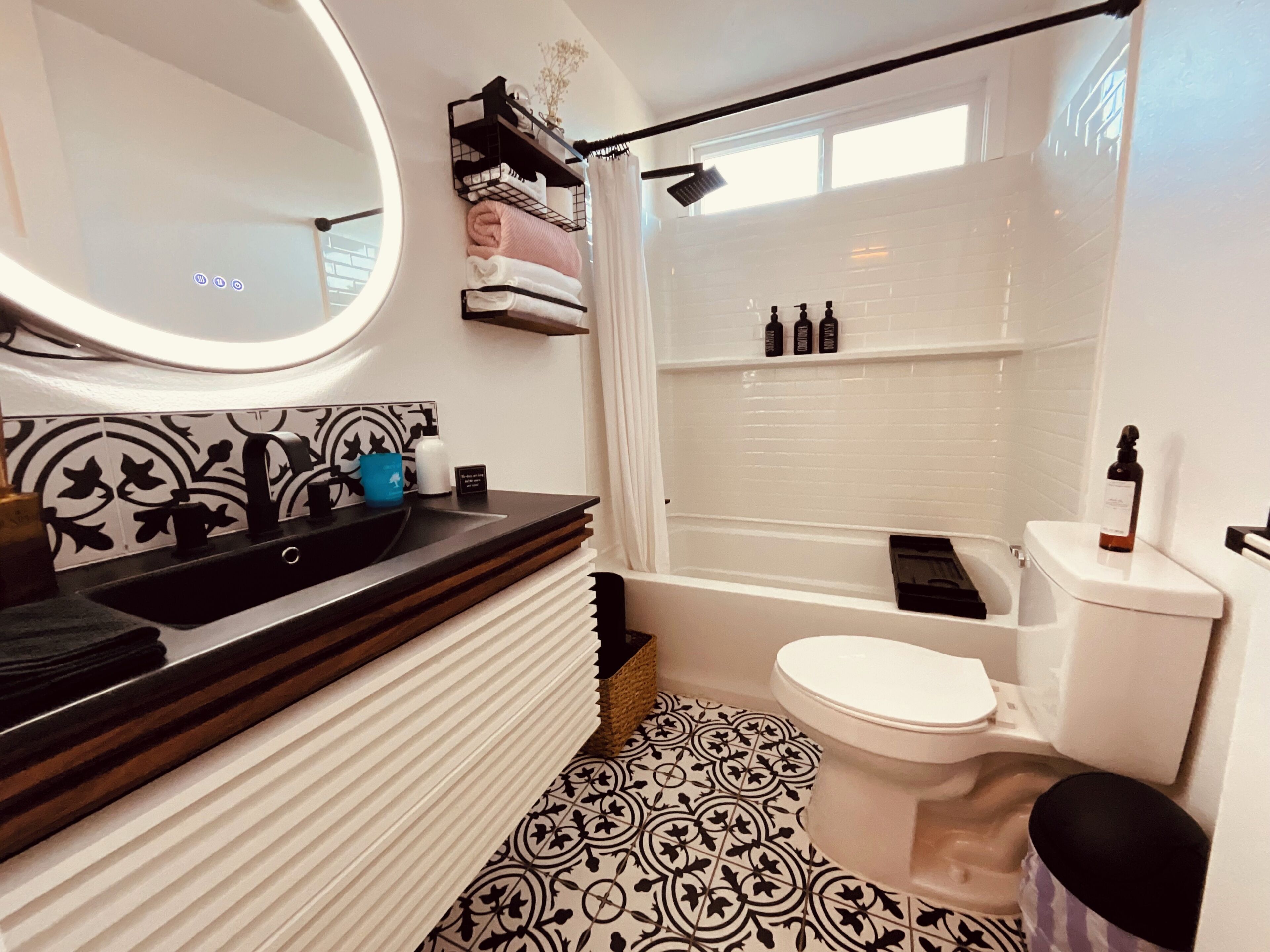 A bathroom with a round mirror, black and white patterned floor, a white toilet, and a shower area.