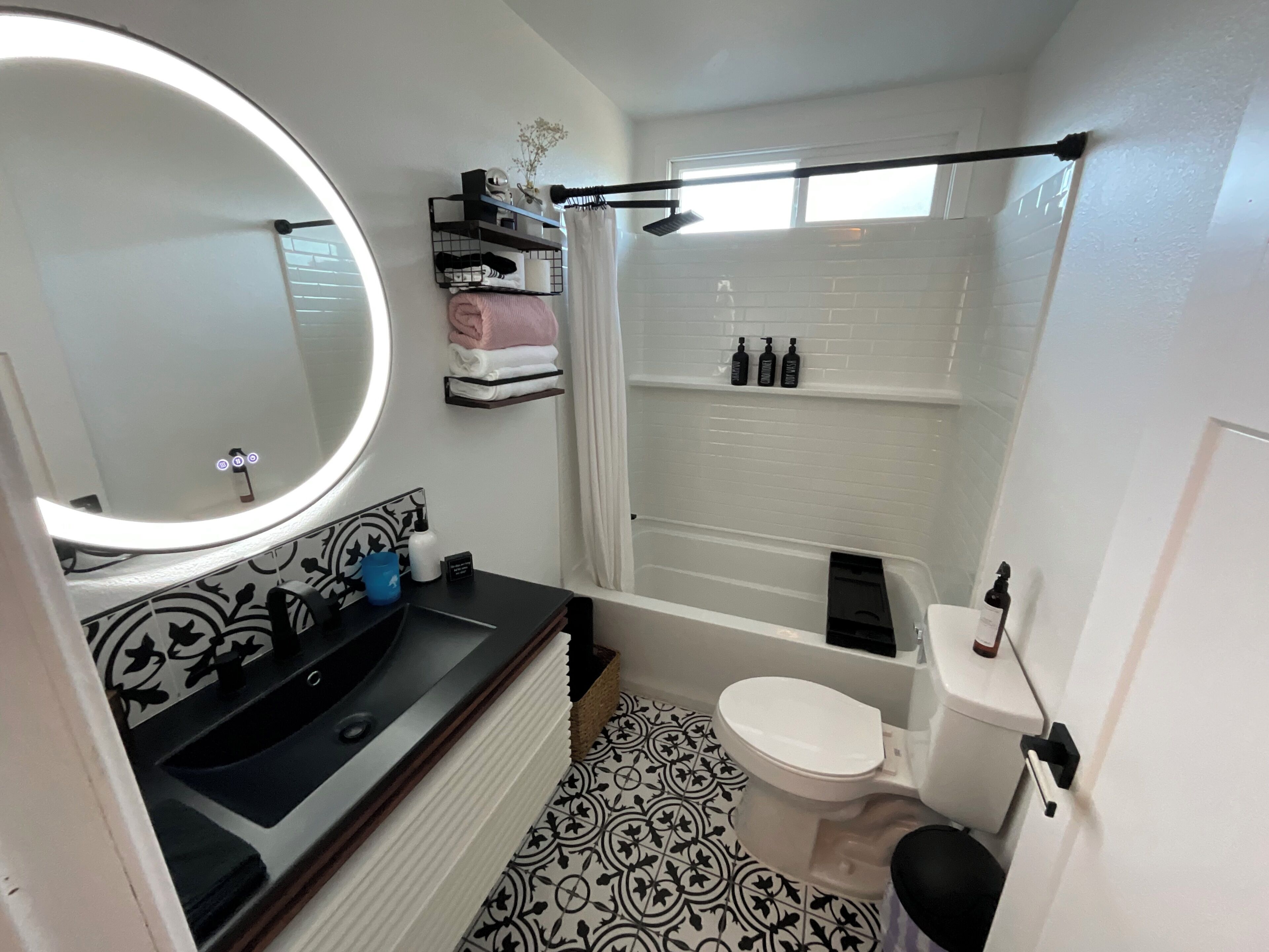 Een badkamer met een ronde spiegel, een wastafel, toilet, douche en een vloer met een patroon.