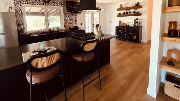 A modern kitchen with a central island, bar stools, a coffee station, and a wooden floor. - Cozy 3-bedroom cabin in charming North Fork with AC (North Fork)