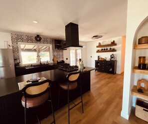 A modern kitchen with a central island, bar stools, a coffee station, and a wooden floor. - Cozy 3-bedroom cabin in charming North Fork with AC (North Fork)