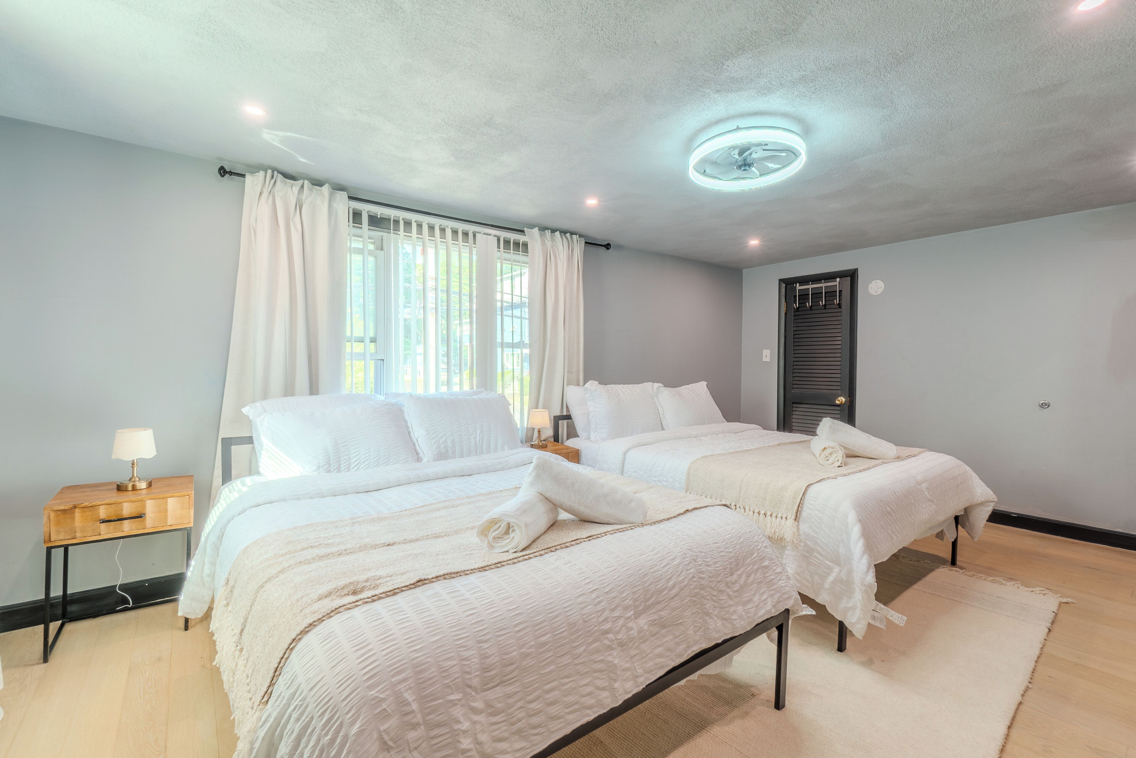 Une chambre avec deux lits, une table de chevet en bois avec une lampe, un ventilateur de plafond et une porte avec une fenêtre.