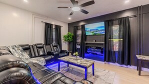 Un soggiorno moderno con un divano componibile, una televisione a schermo piatto, una ventola a soffitto e illuminazione d'ambiente.