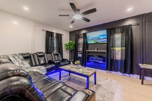 Ein modernes Wohnzimmer mit einer Eckcouch, einem Flachbildfernseher, einem Deckenventilator und stimmungsvoller Beleuchtung.