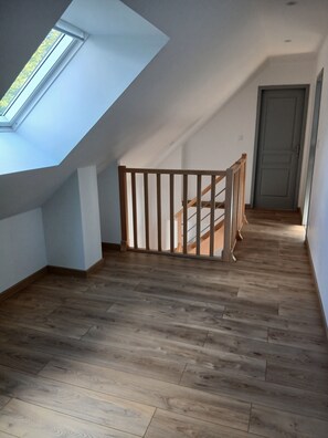 Una habitación amplia con suelo de madera, una escalera de madera y un tragaluz.