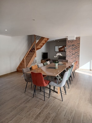 Un espace repas moderne avec une table en bois, plusieurs chaises, un escalier et un mur d’accent en briques.