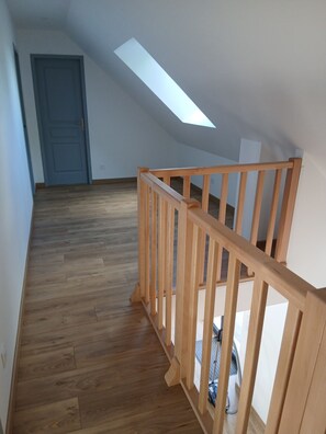 Un escalier en bois avec une rampe, une porte et un puits de lumière dans une pièce dont le sol est recouvert de planches de bois.