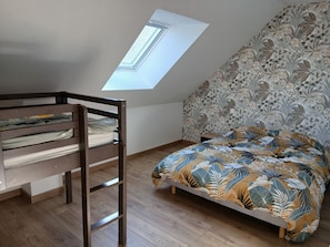 A room with a bunk bed, a skylight, a patterned wall, and a bed with a leaf-patterned bedspread.