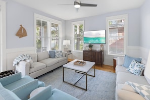 A living room with a sofa, armchairs, a coffee table, a TV, and a fireplace. - Sunset On Laurel – 3BR Golf Retreat, Golf Carts 🛺, Resort Amenities, Pets (Miramar Beach)
