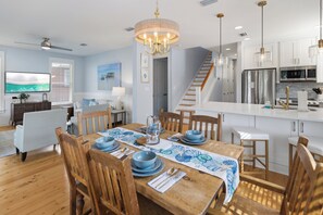A modern kitchen with stainless steel appliances, a wooden dining table set with blue tableware, and a chandelier. - Sunset On Laurel – 3BR Golf Retreat, Golf Carts 🛺, Resort Amenities, Pets (Miramar Beach)