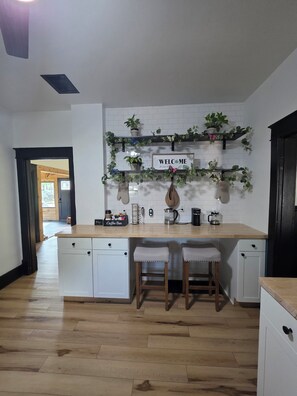 A kitchen with a white countertop, two bar stools, a coffee bar, and a welcome sign.