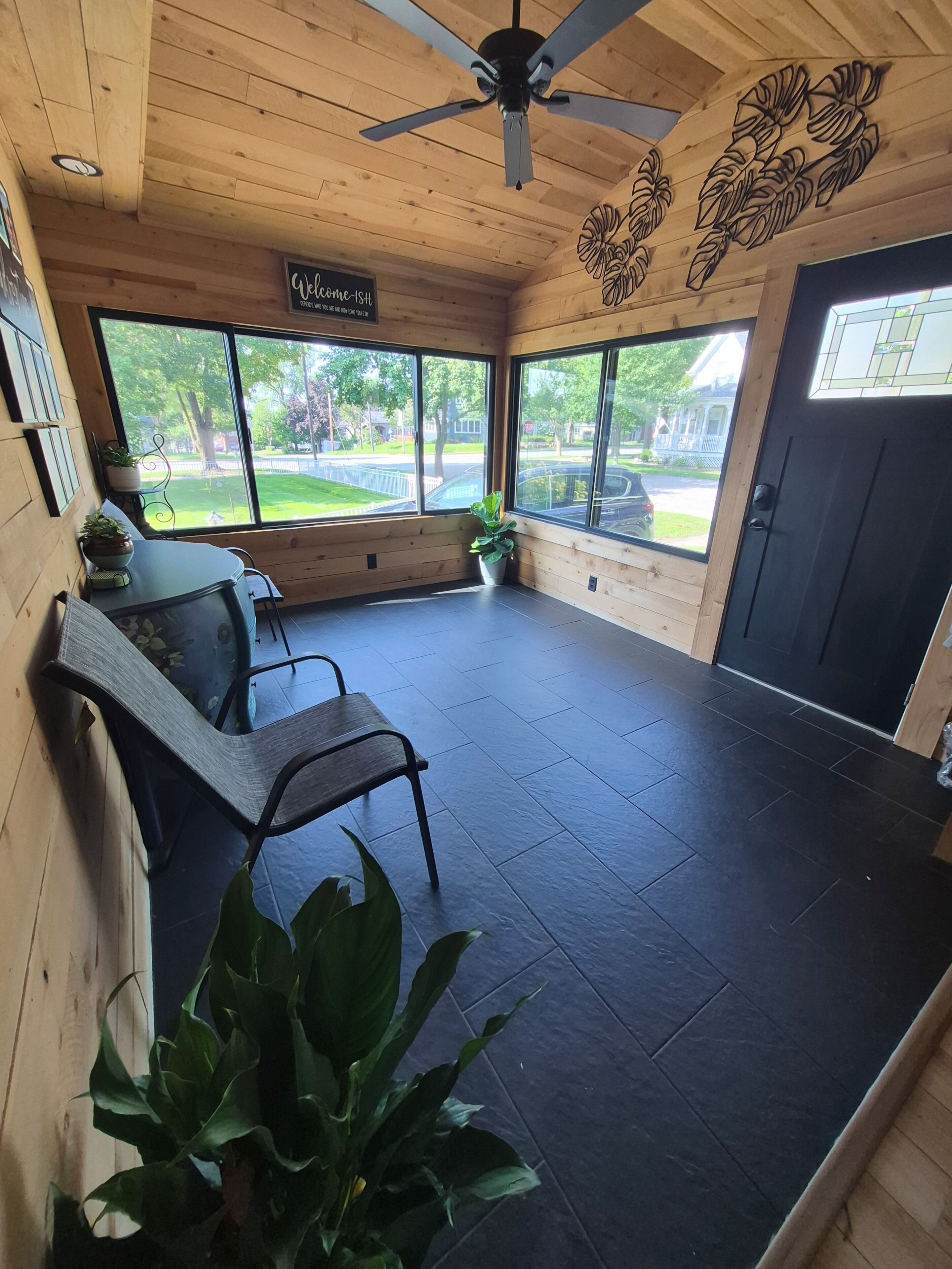 A room with a ceiling fan, a bench, a table with chairs, a potted plant, and a view of the outside.