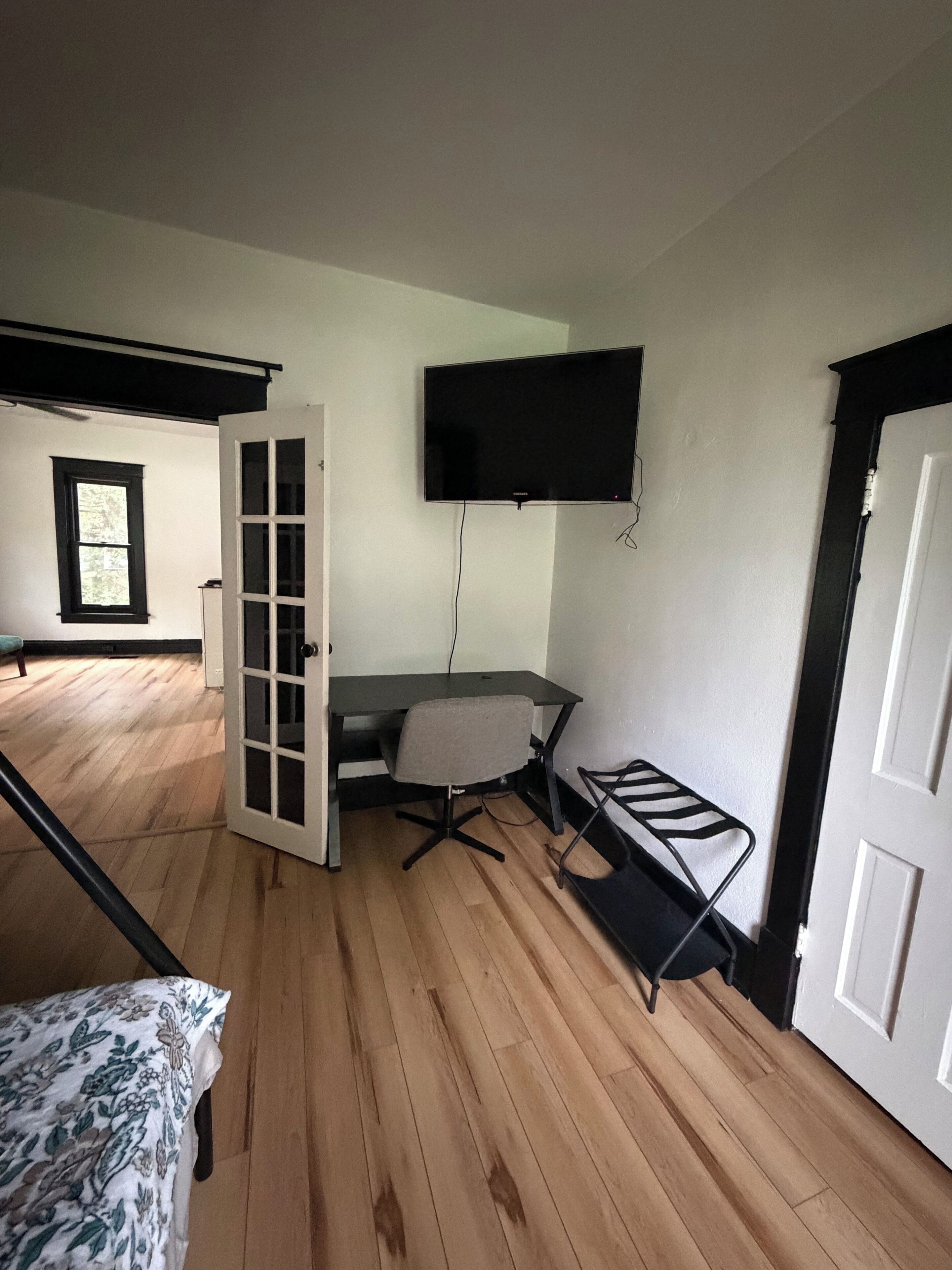Quarto com uma cama, escrivaninha, cadeira, televisão na parede e janela.