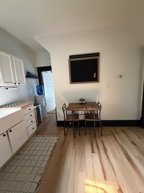 Een keuken met witte kastjes, een houten tafel met stoelen, een waterdispenser en een bord aan de muur.