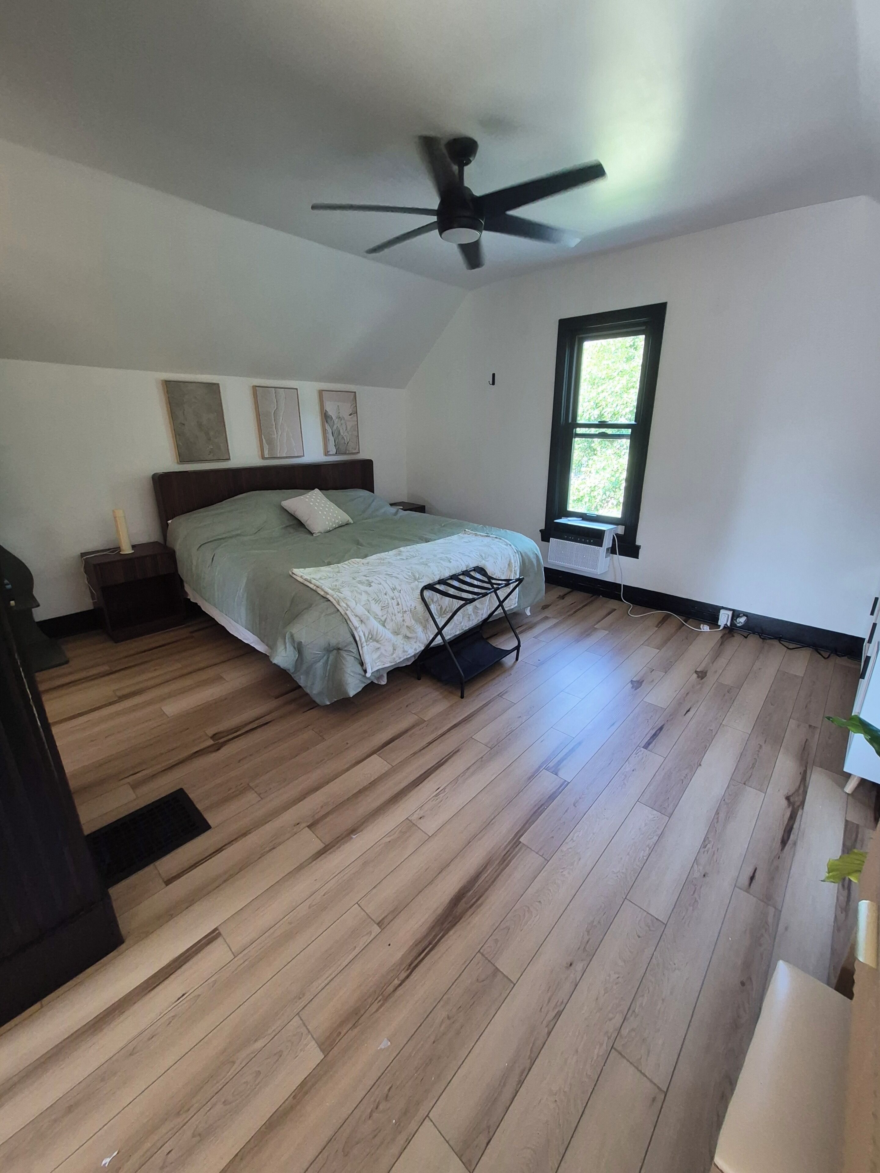 A bedroom with a bed, a ceiling fan, a window, and wooden flooring.