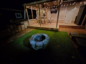 A patio area with a fire pit, outdoor seating, and string lights. - Quaint home that sleeps 9, 3 blocks from the Beach. Private back yard with bar. (Culver)
