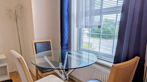 Ein Zimmer mit einem Glastisch, umringt von Holzstühlen, einem Heizkörper und einem Fenster mit Jalousien.
