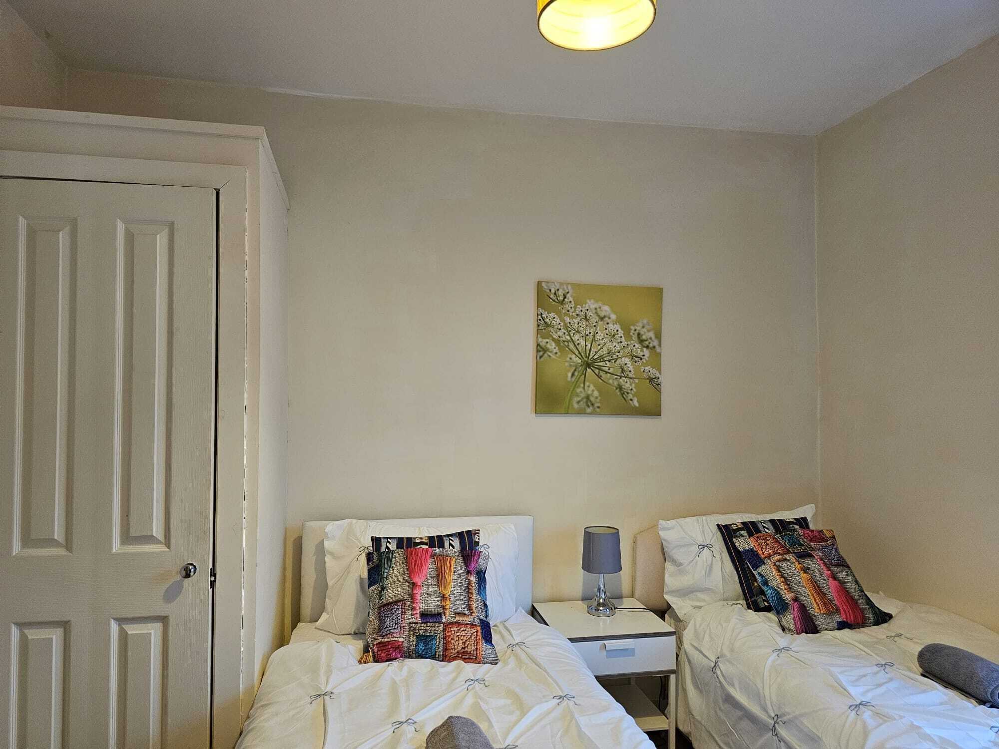 Una stanza con due letti, un comodino, una lampada e un quadro appeso al muro.