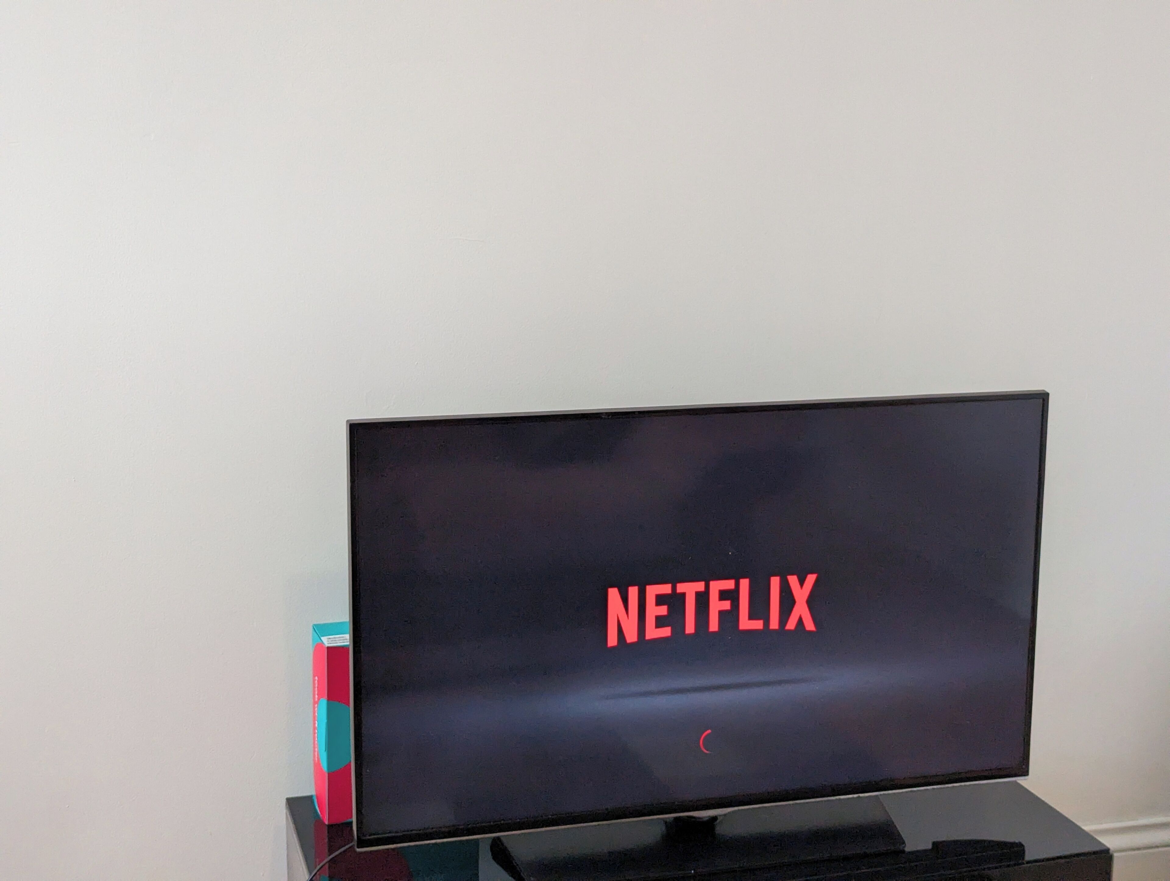 A television with the Netflix logo on its screen, placed on a stand against a plain wall.