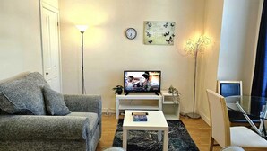 Ein Wohnzimmer mit einer Couch, einem Couchtisch, einem Fernseher, einer Uhr und einer Wandpflanze.