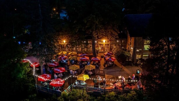 An outdoor dining area with umbrellas and string lights, surrounded by trees and buildings. - Starved Rock Lodge & Conference Center (Oglesby)