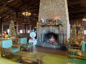 A rustic lodge interior with a stone fireplace, wooden furniture, and Christmas decorations.