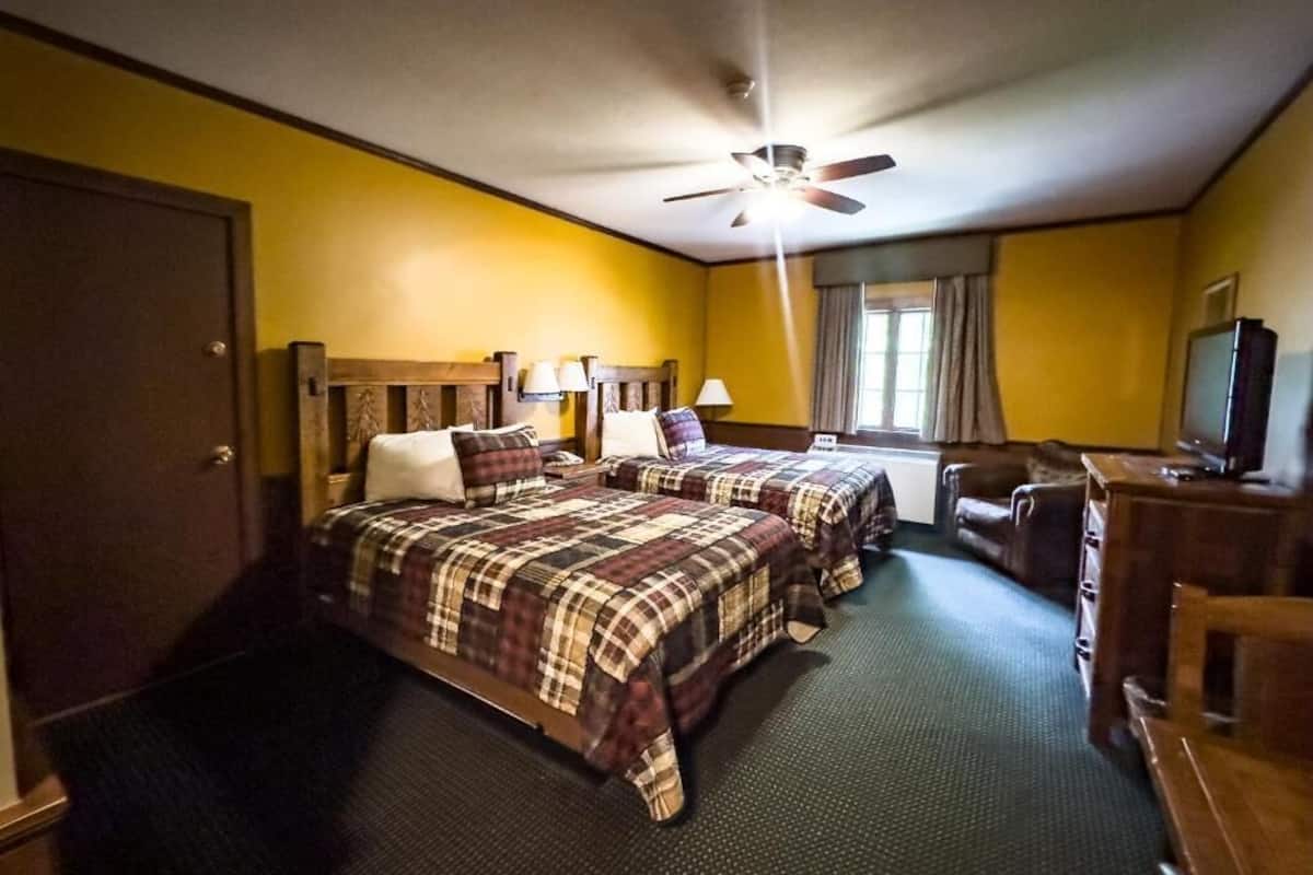 Habitación de hotel con dos camas, un escritorio, un televisor y un ventilador de techo.