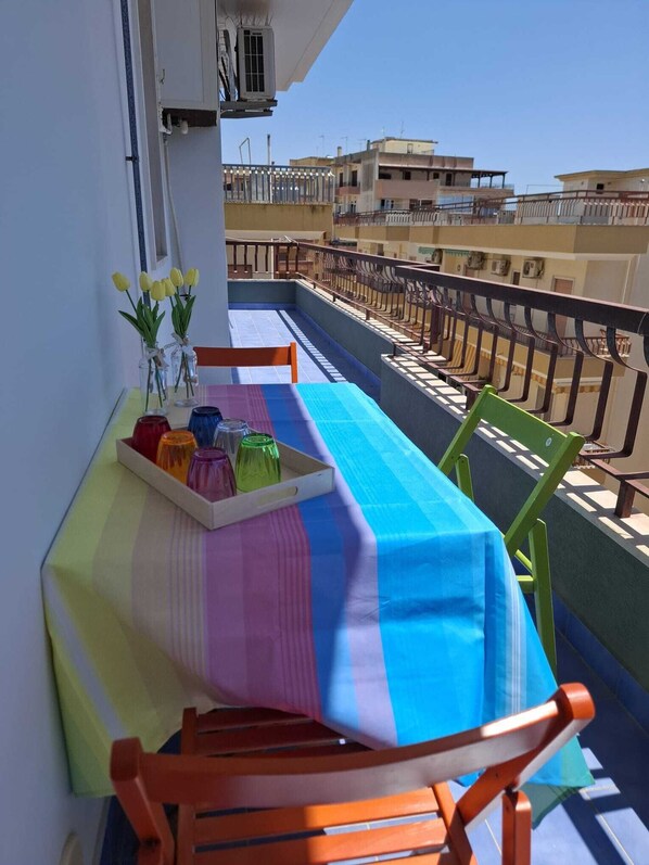 Ein Balkon mit einem Tisch für zwei Personen, einem Stuhl, einer Serviertreppe mit Flaschen und einer Vase mit Blumen.