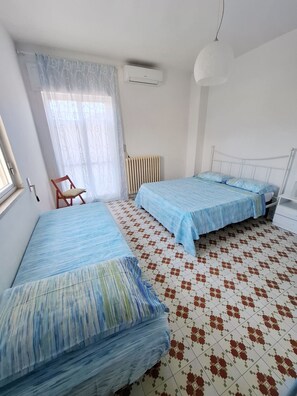 Ein Schlafzimmer mit zwei Betten, einem Heizkörper, einem Fenster mit Vorhängen und einer Hängelampe.