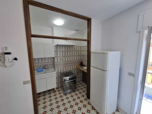Eine kompakte Küche mit Gasherd, weißen Schränken, einem weißen Kühlschrank und Fliesenspiegel mit Muster.