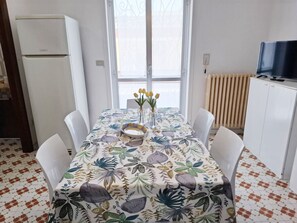 Ein Essbereich mit einem Tisch für zwei Personen, einem weißen Kühlschrank, einer Heizung und einem Fernseher auf einem Schrank.