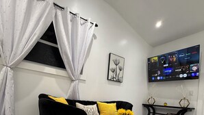 Un salon moderne avec un canapé noir, une table basse ronde, un téléviseur fixé au mur et une fenêtre avec des rideaux.