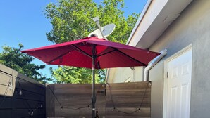 Une terrasse avec deux fauteuils en osier, une table et un parasol rouge.