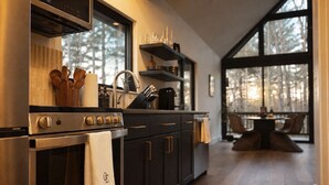 Una cocina moderna con estufa, horno y muebles oscuros. Una ventana ofrece vistas a árboles fuera.