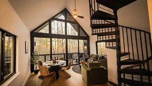 Un interior moderno con una escalera de caracol, ventanas amplias, una zona de comedor con mesa y sillas, y un rincón de estar acogedor.