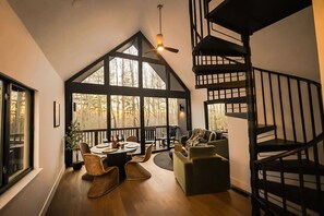 A modern interior with a spiral staircase, large windows, a dining area with a table and chairs, and a cozy seating area. - Cortland Cabin | Grand Opening (Hendersonville)