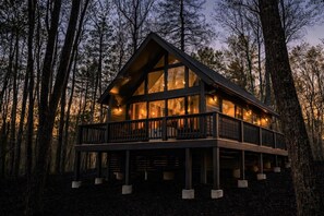 A cabin with a balcony, large windows, and a forest backdrop. - Cortland Cabin | Grand Opening (Hendersonville)
