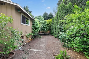 A house with a gravel driveway, a garden with various plants, and a wooden bench.