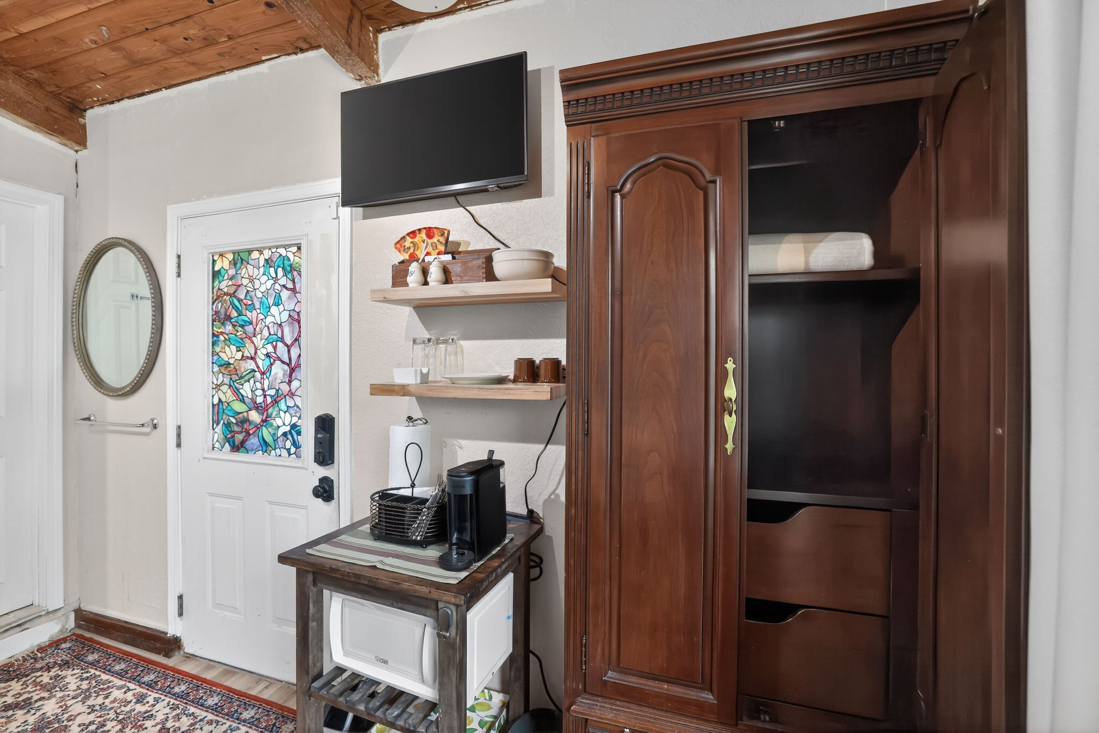A room with a wooden cabinet, a television, a coffee maker, and a decorative glass door.