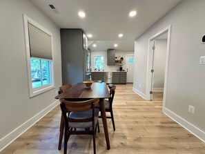 A modern kitchen with a dining area, wooden flooring, and a view of the outdoors.
