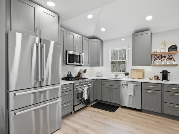 A modern kitchen with stainless steel appliances, grey cabinetry, and a black rug.