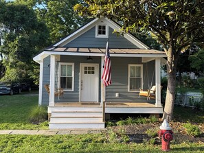 Een klein huis met een veranda, een schommel en een Amerikaanse vlag.