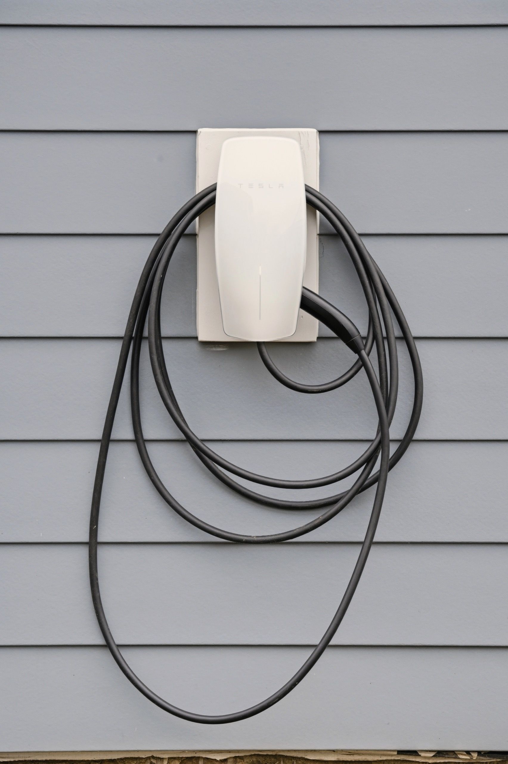 Een wit stopcontact met een zwarte kabel, bevestigd aan een grijze buitenwand.