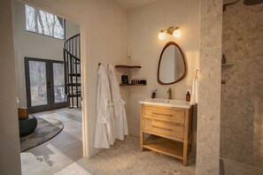 A bathroom with a wooden vanity, a mirror, and a shower area. - Ambrosia Abode | Grand Opening (Hendersonville)